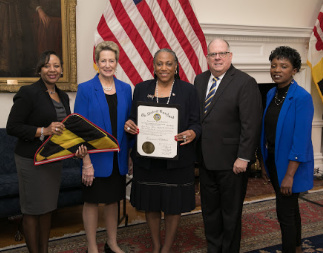 Maryland Governor Larry Hogan, State Superintendent of Schools Dr. Karen B. Salmon with 3 representatives from Glenarden Woods Elementary School holding a certificate and a Maryland flag.