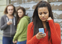 A worried looking teenage girl looks at her phone.