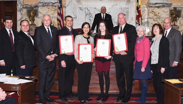 2 men and 2 women holding certificates pose with State legislators in the front of the Maryland General Assembly