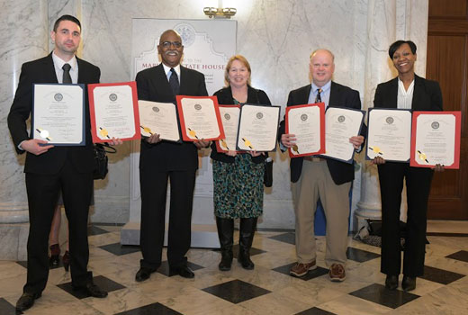 Three men and two women hold certificates in the hallway of the Maryland State House.